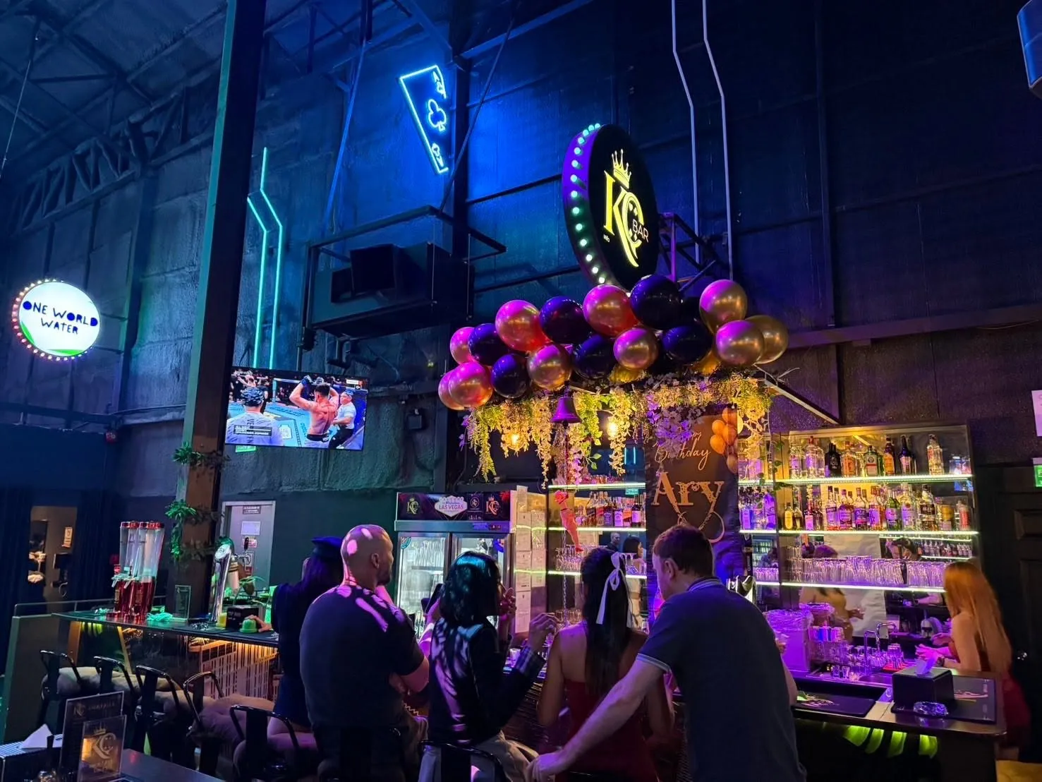 The front of KQ Bar with its marquee sign, the spirits shelf and a screen showing the sport